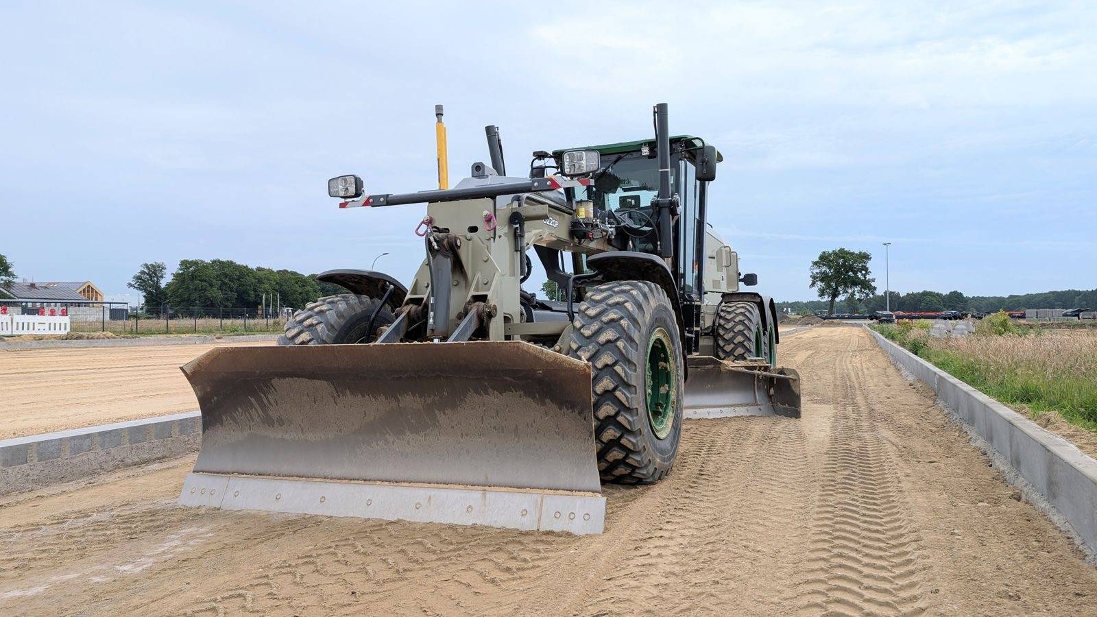 Motor grader leveling a cleared lot to a smooth, build-ready grade with new curbs in place and open sky behind